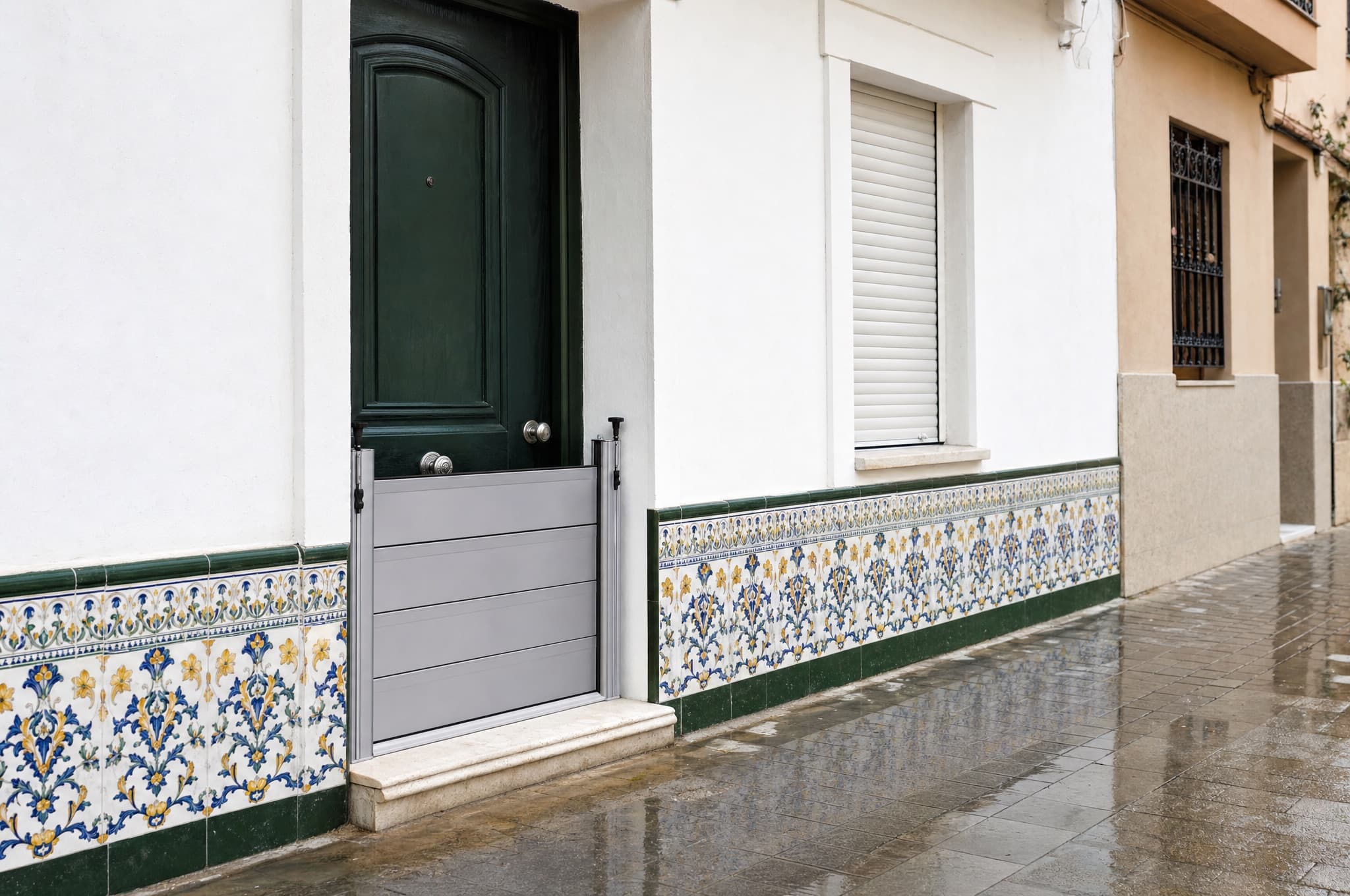 Barrera antiinundación de lamas de aluminio montada en la puerta de una planta baja con zócalo de azulejos valencianos.